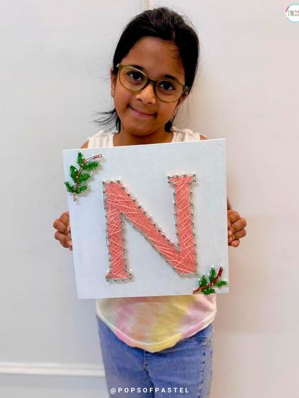 Success. This young girl proudly displays her finished initial 'N' string art, complete with delicate leafy details.