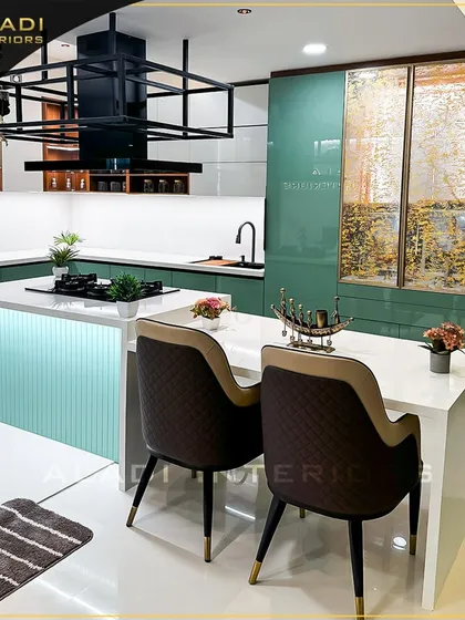This modern kitchen is the heart of the home, featuring a mint-green island with an integrated cooktop and a breakfast bar. The design combines functionality with style, including a custom overhead rack for storage and display, and high-end quilted dining chairs.