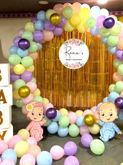 A pastel-themed baby shower decoration with a gold fringe backdrop. The setup includes cute baby cutouts and 'BABY' blocks.