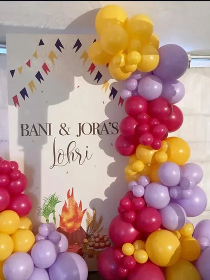 A colorful balloon arrangement I made for Bani & Jora's Lohri party. The custom backdrop with the bonfire graphic is flanked by bright balloon pillars in yellow, pink, and purple.