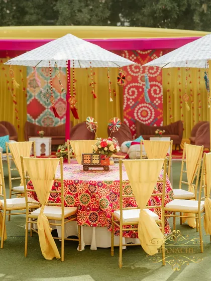 Guest seating featuring tables draped in vibrant phulkari-inspired linen. The backdrop includes traditional printed panels, creating a cohesive and colorful look.