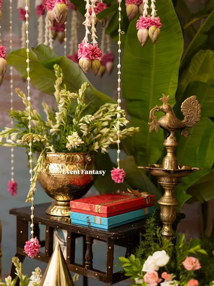 A detail shot showing the combination of brass props, like the Annapakshi lamp, and fresh flowers. The hanging lotus bud garlands and banana leaves complete this classic South Indian decor look.
