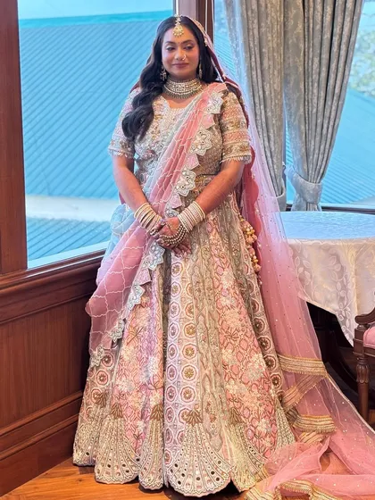 A full-length view of the bride in her unique pastel blue and pink lehenga. The makeup is soft and romantic to match the outfit's aesthetic.