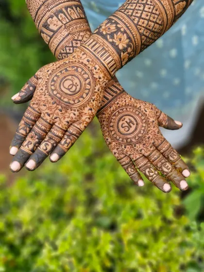 A highly detailed engagement mehendi with the couple's initials 'SH' and 'RS' hidden within the intricate patterns. The design features circular mandalas and interlocking rings.