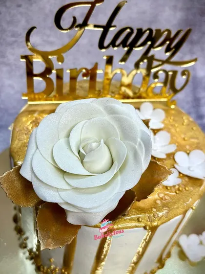 A close-up of a white and gold themed cake, highlighting the handmade white sugar rose and delicate gold details.