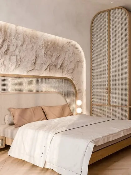 We create bedrooms that feel like a homecoming to calm. This space uses a palette of natural textures, including a raw stone feature wall with soft backlighting and a headboard blending cane and fabric, to craft a sanctuary of quiet luxury.