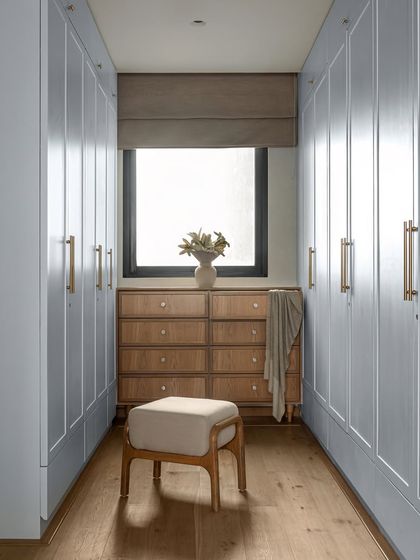 The walk-in closet in the KAIA master bedroom was designed to feel calm and functional. His-and-her wardrobes are finished in a soft blue that echoes the bedroom's highlights, while a custom wooden dresser sits under the window, bringing in natural light and a sense of grounded luxury.
