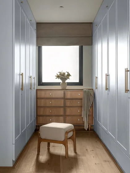 The walk-in closet in the KAIA master bedroom was designed to feel calm and functional. His-and-her wardrobes are finished in a soft blue that echoes the bedroom's highlights, while a custom wooden dresser sits under the window, bringing in natural light and a sense of grounded luxury.