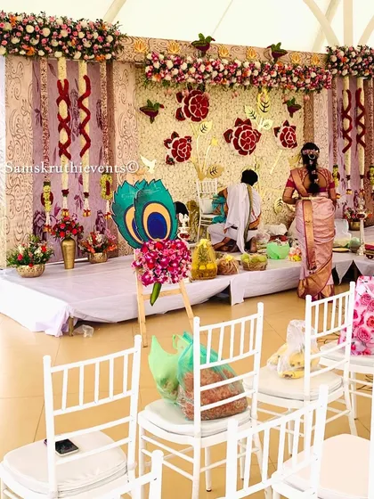 A beautiful outdoor naming ceremony with a backdrop of white flowers and golden rose motifs. The setup includes white chairs for guests, creating an elegant and serene atmosphere.