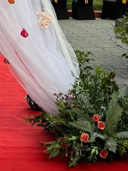 The base of the bow entrance arch, showing how the greenery and floral arrangements ground the large structure and tie it into the red carpet entrance.
