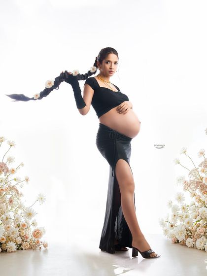 A contemporary and stylish shot showcasing a bare bump with a modern black outfit. The floral arrangements on either side frame the portrait beautifully, blending modern style with classic elegance.