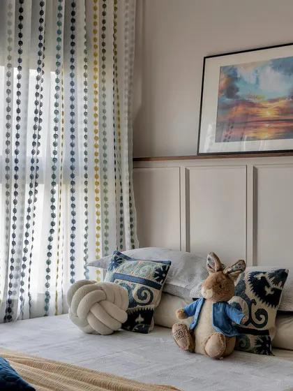 A sweet and cozy corner of the kids' room. The bed is styled with patterned pillows and a stuffed rabbit, set against a backdrop of paneling and a beautiful sunset painting.