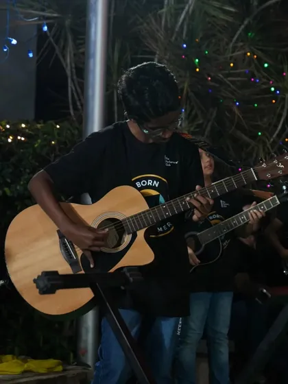 A student confidently performing on his acoustic guitar, set up with a microphone to share his music with the crowd.