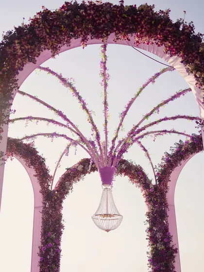 A close-up of the ceremony's centerpiece: a stunning floral chandelier suspended within the main arch. The design combines architectural structure with the softness of purple flowers, creating a focal point of dramatic beauty.