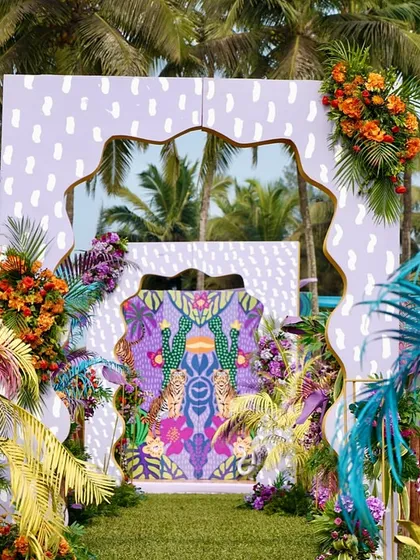 The grand entrance to a tropical carnival event, with layers of colorful backdrops, exotic florals, and palm trees.