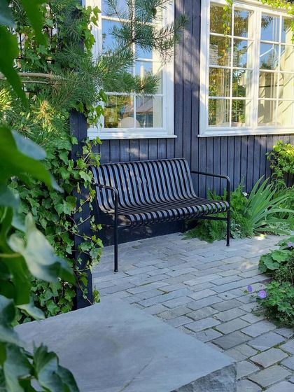 A cozy seating nook with a modern metal bench set on a cobblestone patio. We use climbing ivy and lush border plants to soften the hardscaping and create a sense of enclosure.