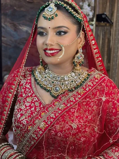 A beautiful portrait of a bride in a traditional red lehenga and dupatta. The makeup is focused on creating a flawless base and highlighting the eyes and lips to complement the heavy jewelry.