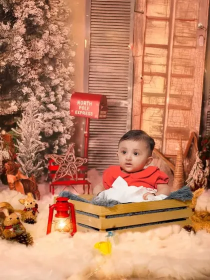 A cozy Christmas-themed studio shoot. The setup includes a snowy backdrop, festive trees, and warm lights to create a magical holiday portrait.