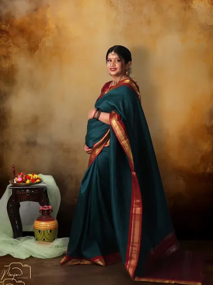 A full-length portrait in a stunning green saree, against a classic painted backdrop.
