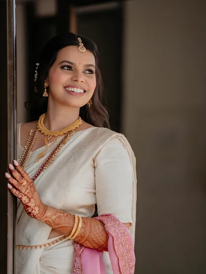 A dreamy, looking-away shot that highlights the bride's elegant side profile. The makeup is soft and timeless, perfect for her classic white and gold saree.