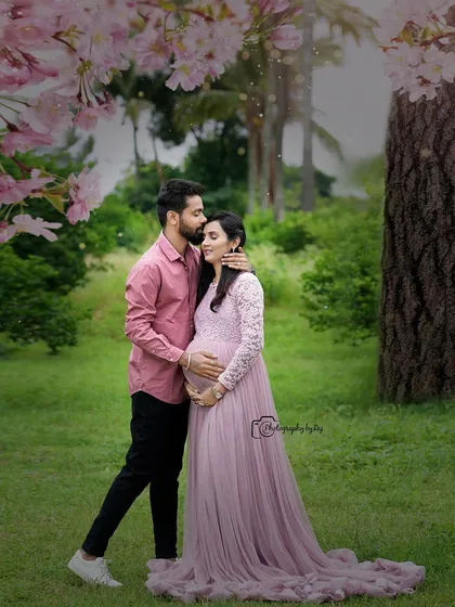 A romantic couple's portrait under a tree with pink blossoms. The mother-to-be's pink lace gown is perfect for this dreamy setting.