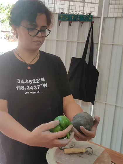 A student fully absorbed in her work, comparing her clay sculpture to the real bell pepper. This focused state is a form of active meditation.