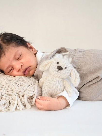 The classic 'tushy up' pose is a newborn favorite. Here, the baby is cuddling a small knitted toy, adding a touch of sweetness.
