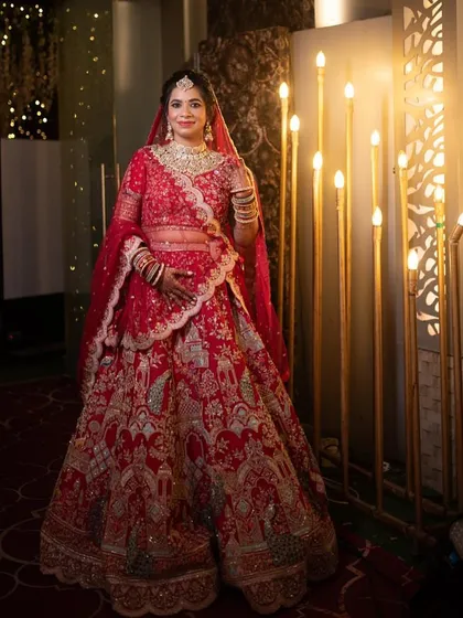 A full-length portrait of the bride in her stunning red lehenga. The makeup is classic and traditional, with a focus on radiant skin and defined features.