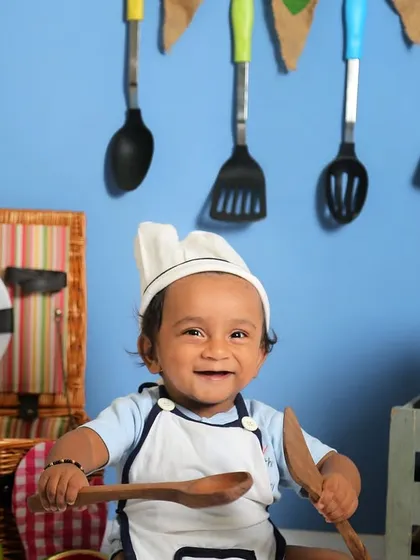 A happy little chef playing with wooden spoons. The bright blue background contrasts beautifully with the colorful props in this fun sitter session.