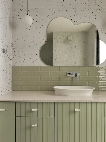 We designed this kids' bathroom with playful yet stylish elements. A sage green vanity with reeded doors is paired with a terrazzo-effect wall and a unique cloud-shaped mirror.