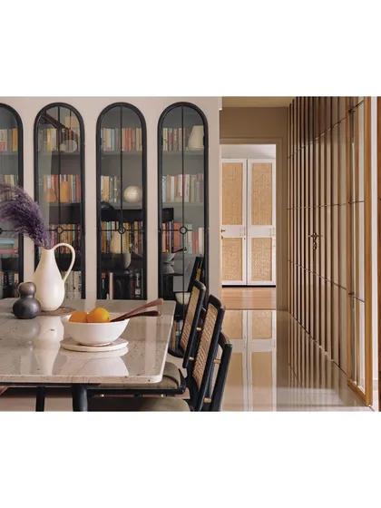 This dining room is inspired by the natural world outside. The space features arched bookshelves and a passage clad in a Shoji-inspired screen, which discreetly hides doors and storage. The design creates a seamless flow and an illusion of length in this 950 sq ft compact apartment.