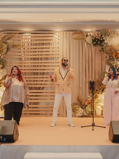 A live band performing on a beautifully designed stage with a rustic, slatted wood backdrop and delicate floral arches, setting a relaxed and happy mood.