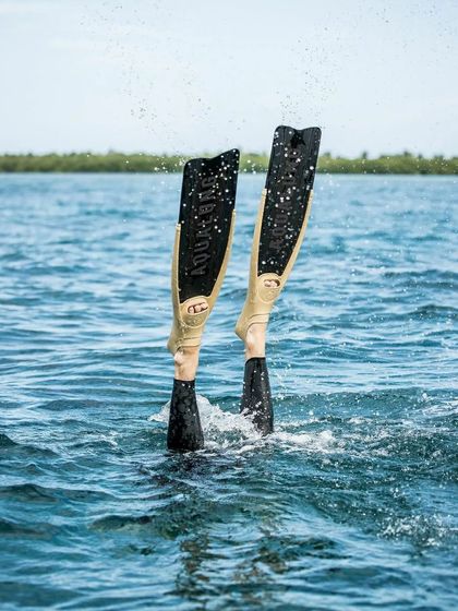 A freediver's legs break the surface, showcasing the powerful thermoplastic blades of the Aqualung Cyclone X fins. This design provides efficient power transfer from the soft rubber foot pockets, propelling the diver with minimal effort.