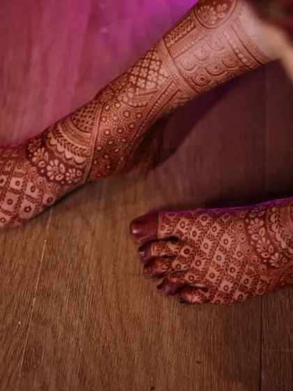 A close-up of the bride's feet, showing the rich stain of the intricate leg mehendi. The pattern is dense and covers the entire foot.