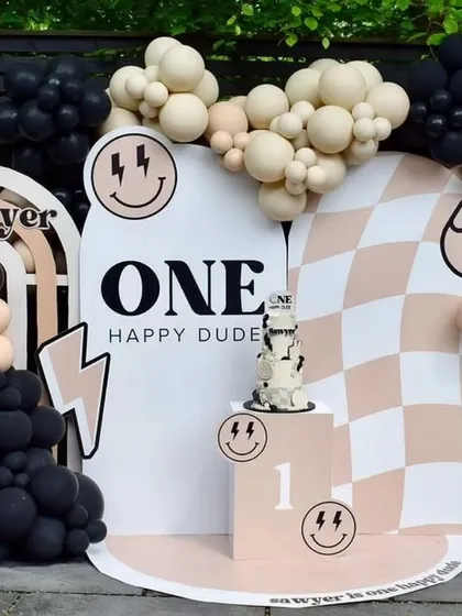 A trendy "One Happy Dude" first birthday theme. This cool setup uses a neutral color palette with black accents, checkerboard patterns, and smiley face icons for a modern and fun vibe.