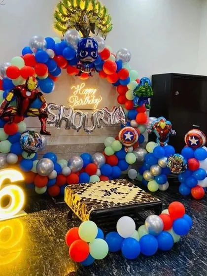 An exciting Avengers-themed birthday decoration for a 6th birthday. This setup includes character cutouts, a neon sign, and a balloon arch in superhero colors.