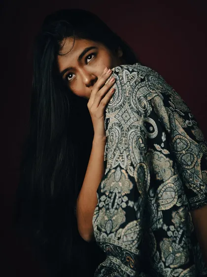 A shy and mysterious pose, with the model partially hiding behind her clothing.