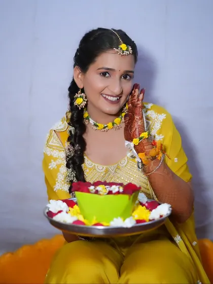 A happy bride-to-be at her Haldi ceremony, holding a platter of flowers, her smile as bright as her outfit.