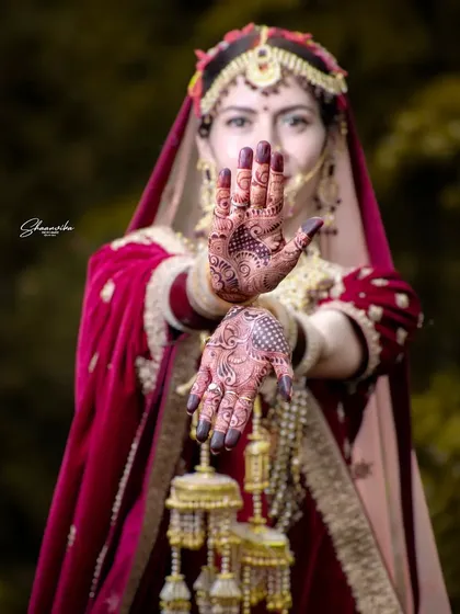 A beautiful bridal portrait showing off the intricate mehndi design. The natural, out-of-focus background makes the bride and her henna art the center of attention.