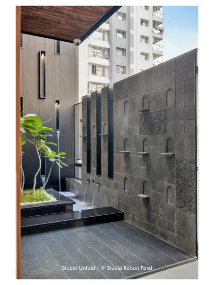 The entrance courtyard of the 'Soham' residence features a dramatic water wall with carved niches, creating a tranquil and impressive arrival experience.