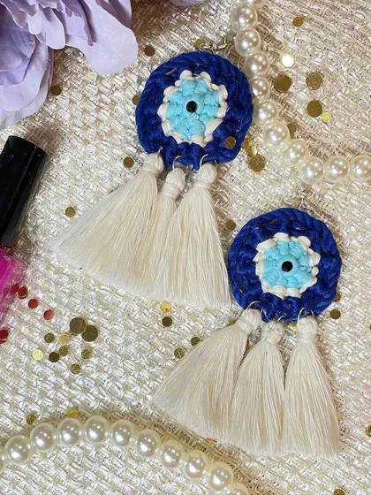 My popular Evil Eye macrame earrings, designed to be both a stylish accessory and a symbol of protection. This close-up shows the detailed knotting in concentric circles of blue, white, and turquoise, finished with three delicate off-white tassels.