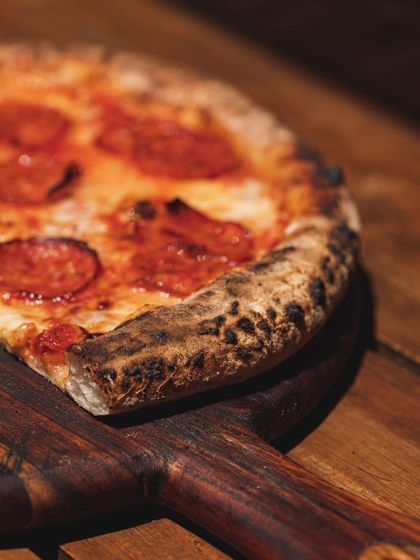 A classic pepperoni pizza, hot out of the wood-fired oven. The crust is blistered and charred, and the pepperoni is perfectly crisped at the edges.