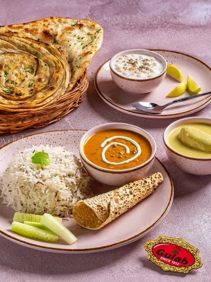 A complete North Indian thali from Gulab Sweets, featuring dal, paneer, raita, rice, and breads on a modern pink plate.