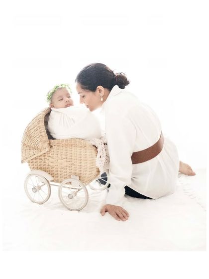 Tiny toes and rosy cheeks. A mother leans over her newborn, who is nestled in a charming wicker pram, a sweet and classic setup for a newborn photoshoot.