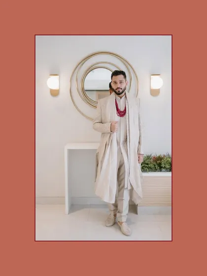A stylish portrait of the groom in a sophisticated, layered sherwani, posing against a modern, minimalist background.