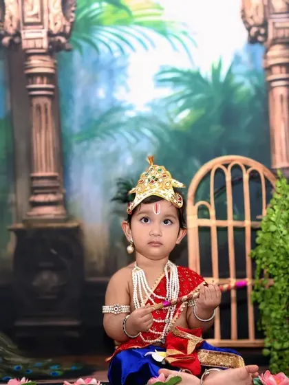 This little Krishna looks thoughtfully to the side, holding his flute in a lush, jungle-like temple setting.