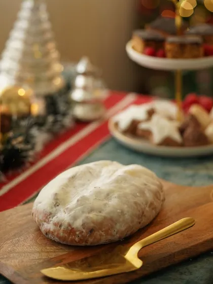 A traditional Christmas stollen bread, dusted with powdered sugar and ready to be sliced, set against a festive background.