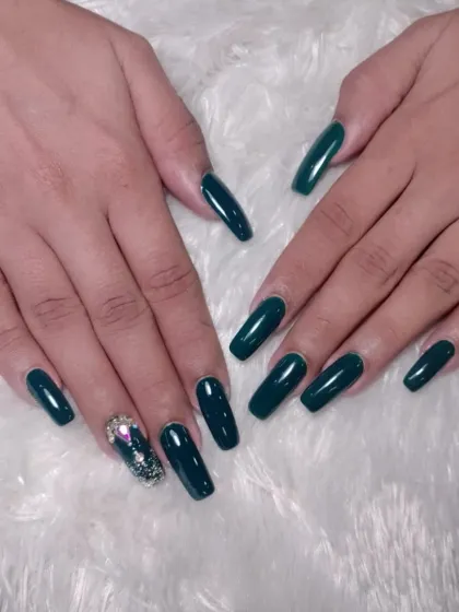 A deep, emerald green set of coffin-shaped extensions with a stunning, fully embellished accent nail using various rhinestones.