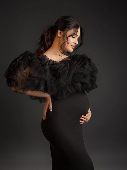 A beautiful solo portrait in a dramatic black ruffled gown, looking down at her bump with love.