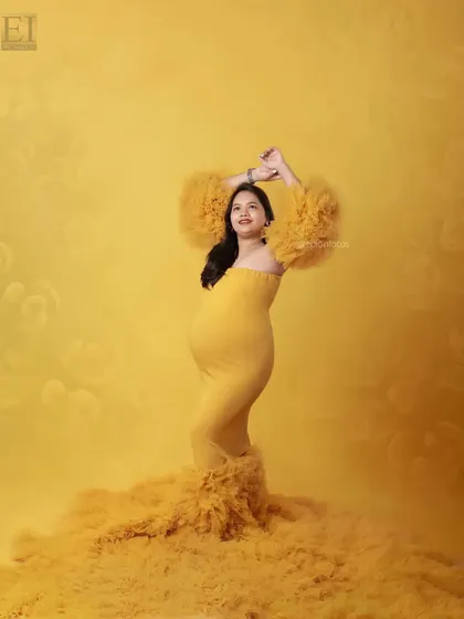 A vibrant studio portrait with the mom-to-be in a sunshine-yellow gown, her arms raised in a joyful pose.